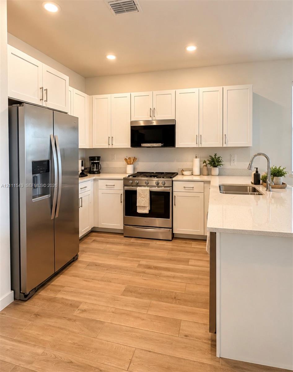 Kitchen featuring white Shaker-style cabinetry, stainless steel appliances, quartz countertops, an undermount sink, and wood-finish flooring