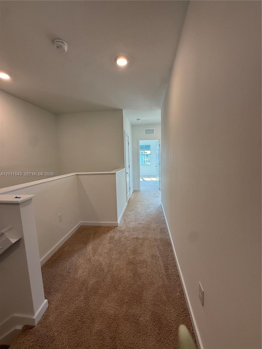 Hallway featuring neutral-toned carpeting, recessed ceiling lighting, and crisp white wall finishes