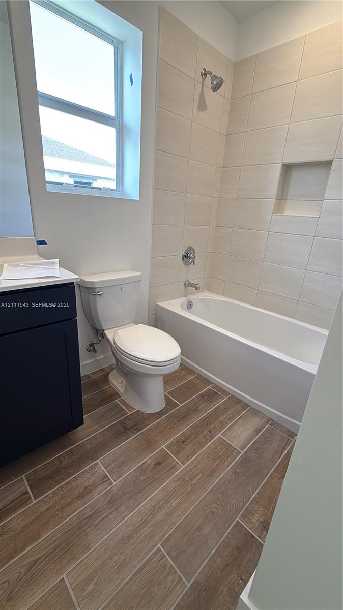 Bathroom featuring wood-finish floor tile, deep-toned vanity cabinet, integrated shower niche, and light-toned wall tile surrounding the bathtub
