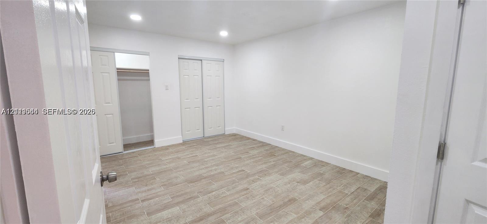 Neutral interior space featuring wood-finish tile flooring, recessed lighting, and dual reach-in closets with six-panel doors Neutral interior space featuring wood-finish tile flooring, recessed lighting, and dual reach-in closets with six-panel doors