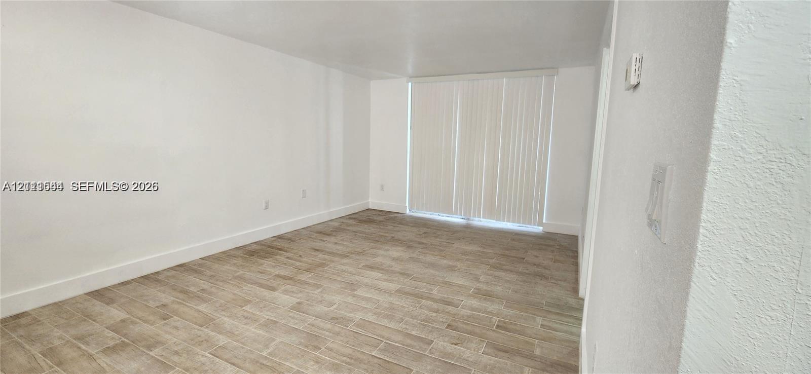 Interior room featuring neutral wall paint, wood-finish tile flooring, and vertical window blinds