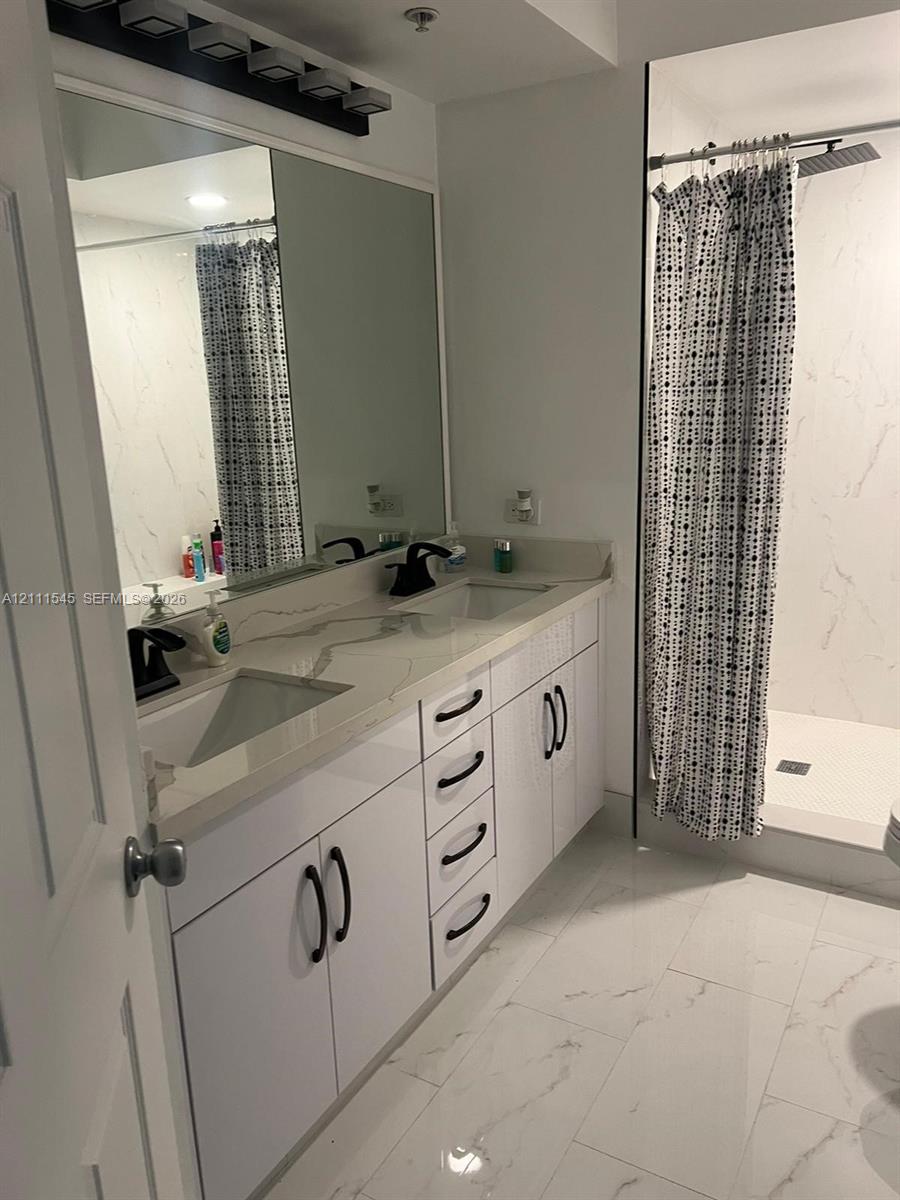 Double vanity featuring white cabinetry, quartz-surface countertops, dual rectangular undermount sinks, matte black hardware, and large-format tile flooring Double vanity featuring white cabinetry, quartz-surface countertops, dual rectangular undermount sinks, matte black hardware, and large-format tile flooring