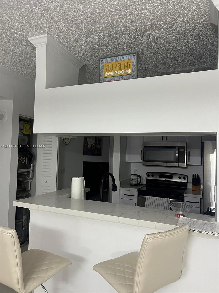 Kitchen featuring a white stone-surface breakfast bar, matte black faucet, white cabinetry, and stainless steel appliances Kitchen featuring a white stone-surface breakfast bar, matte black faucet, white cabinetry, and stainless steel appliances