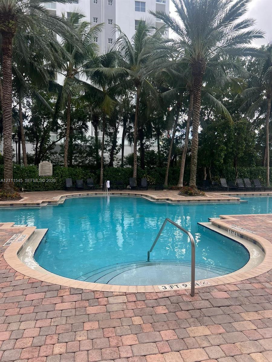 In-ground swimming pool featuring a curved entry with stainless steel handrail, surrounded by brick paver decking, established palm trees, and perimeter landscaping In-ground swimming pool featuring a curved entry with stainless steel handrail, surrounded by brick paver decking, established palm trees, and perimeter landscaping