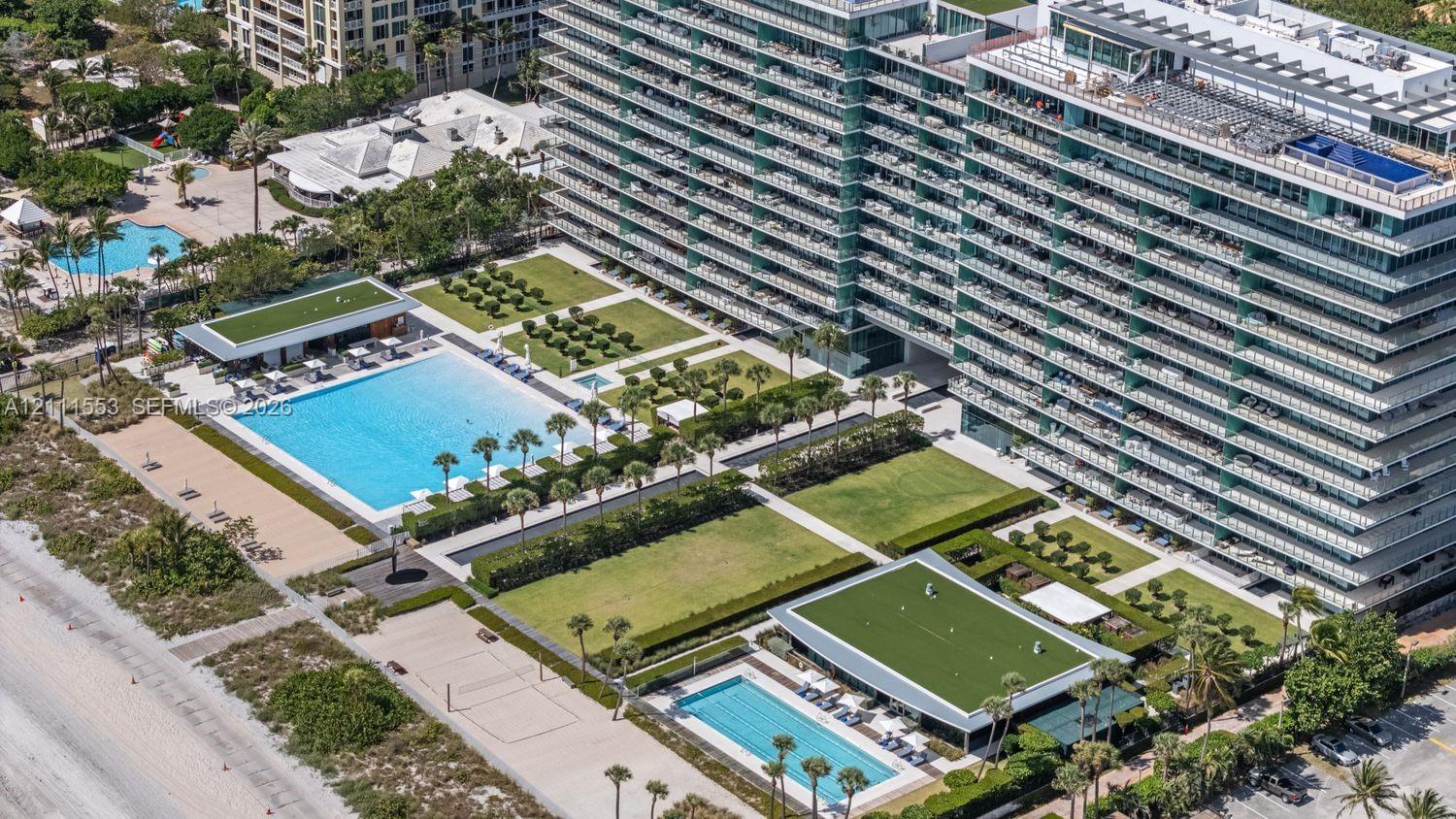High-rise architectural exterior featuring glass-paneled balconies, dual swimming pools, manicured green space, and direct coastal proximity