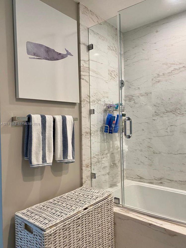 Walk-in shower enclosure featuring floor-to-ceiling stone-look wall tiles, a glass door, and polished chrome hardware, complemented by a wall-mounted metal towel rack