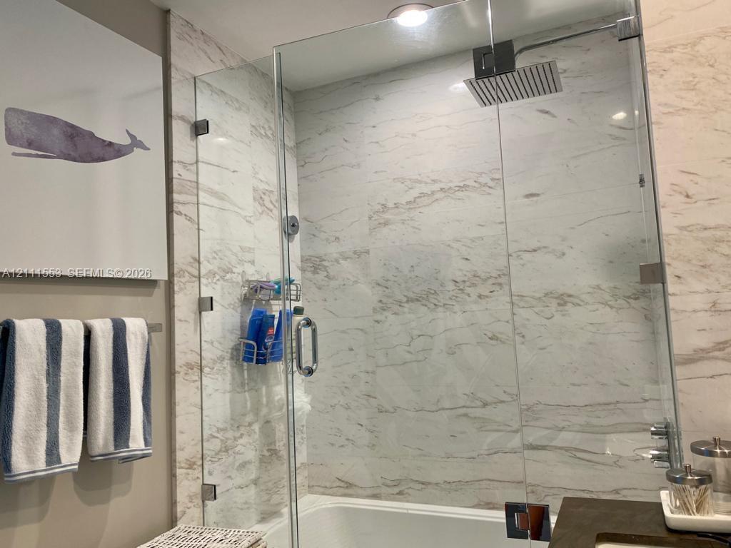 Walk-in shower featuring floor-to-ceiling stone-finish tile surround, a frameless glass enclosure, and a ceiling-mounted rainfall showerhead