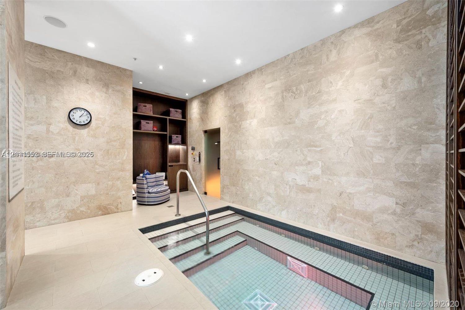 Indoor plunge pool featuring stone wall cladding, recessed lighting, built-in shelving, and a metal handrail