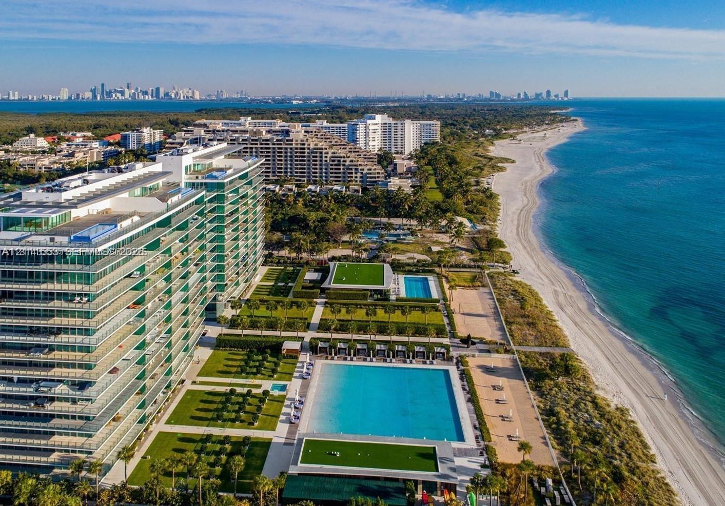 Direct oceanfront high-rise featuring expansive swimming pools, structured landscaping, manicured lawn areas, and sand beach access