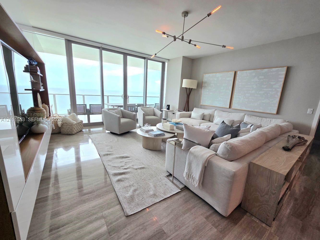 Floor-to-ceiling sliding glass doors, polished stone flooring, integrated wood-finish cabinetry, and contemporary multi-arm chandelier