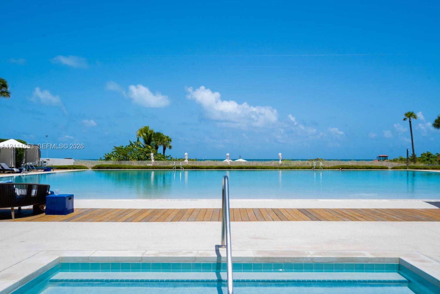 Pool with wood-plank decking, concrete pool surround, built-in spa with tile lining, and metallic handrails