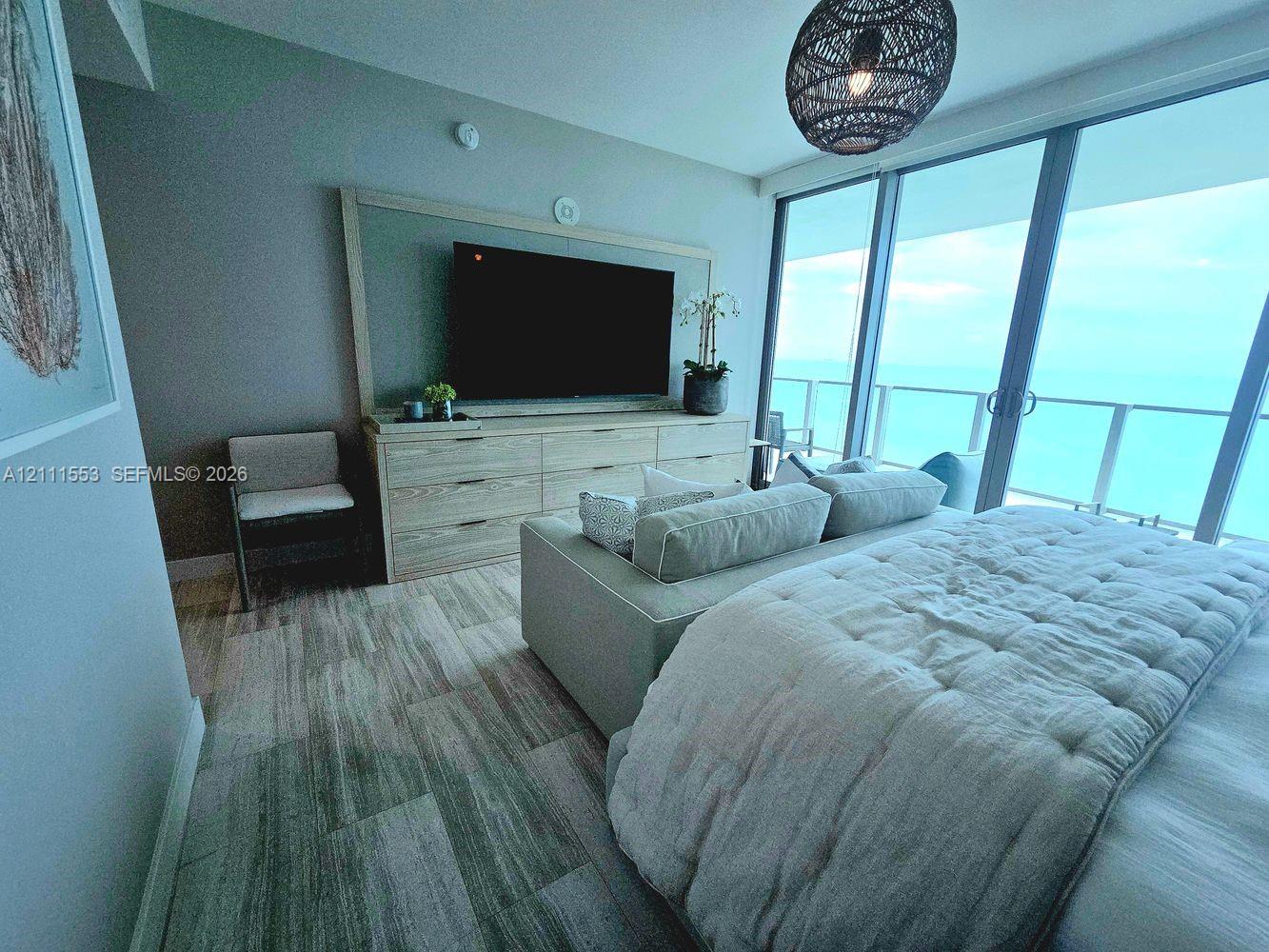 Floor-to-ceiling glass sliding doors, wood-finish tile flooring, built-in light-tone cabinetry, and a private balcony