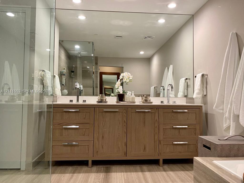 Double vanity featuring natural wood-finish cabinetry, chrome hardware, recessed lighting, and a full-width wall mirror
