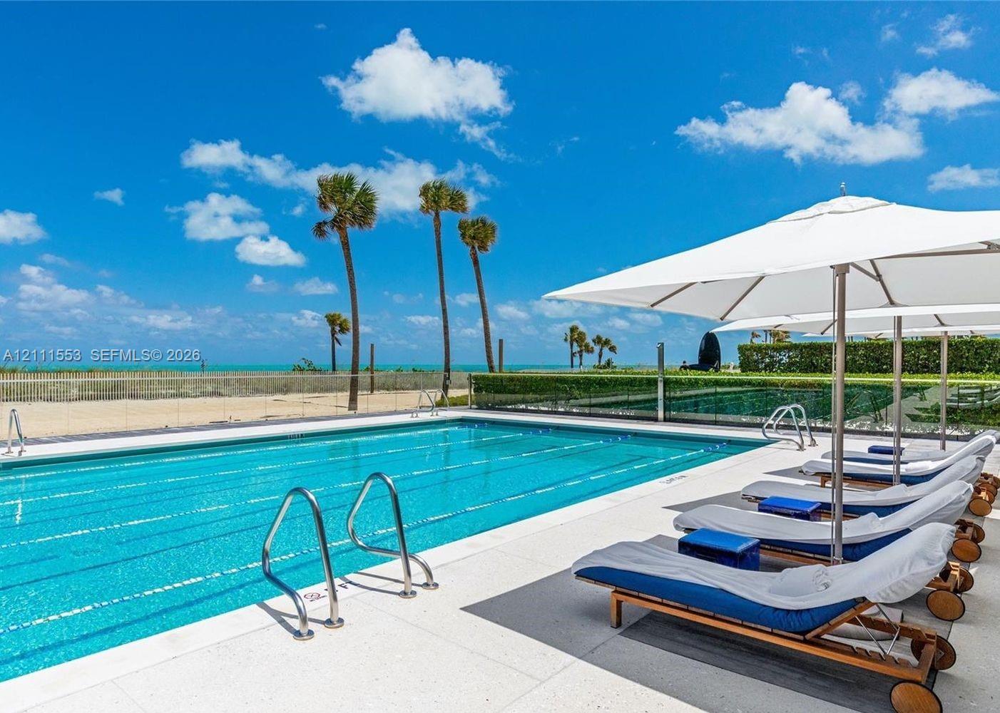 Rectangular lap pool featuring a concrete deck, metal handrails, and a glass perimeter fence