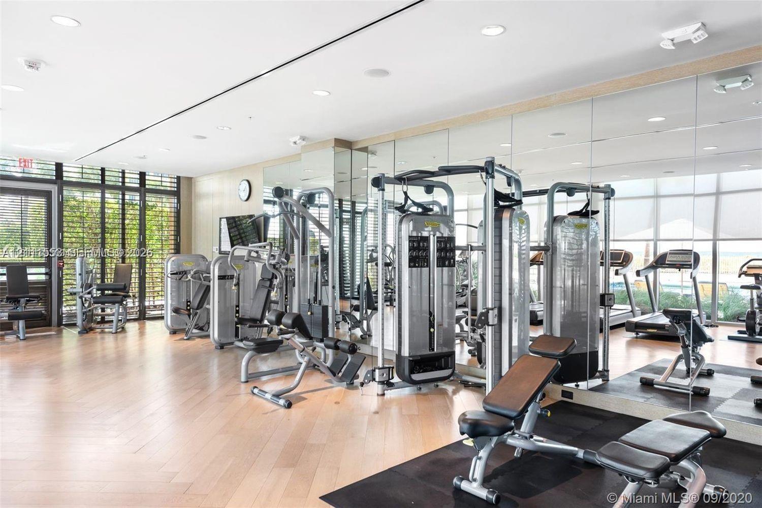 Fitness facility featuring wood-finish flooring, floor-to-ceiling mirrored walls, recessed lighting, and expansive windows