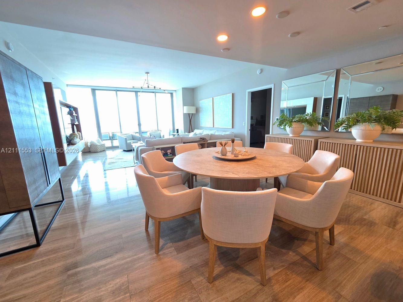 Open-concept living space featuring wood-finish flooring, recessed lighting, expansive floor-to-ceiling windows, and dual built-in slatted cabinetry units
