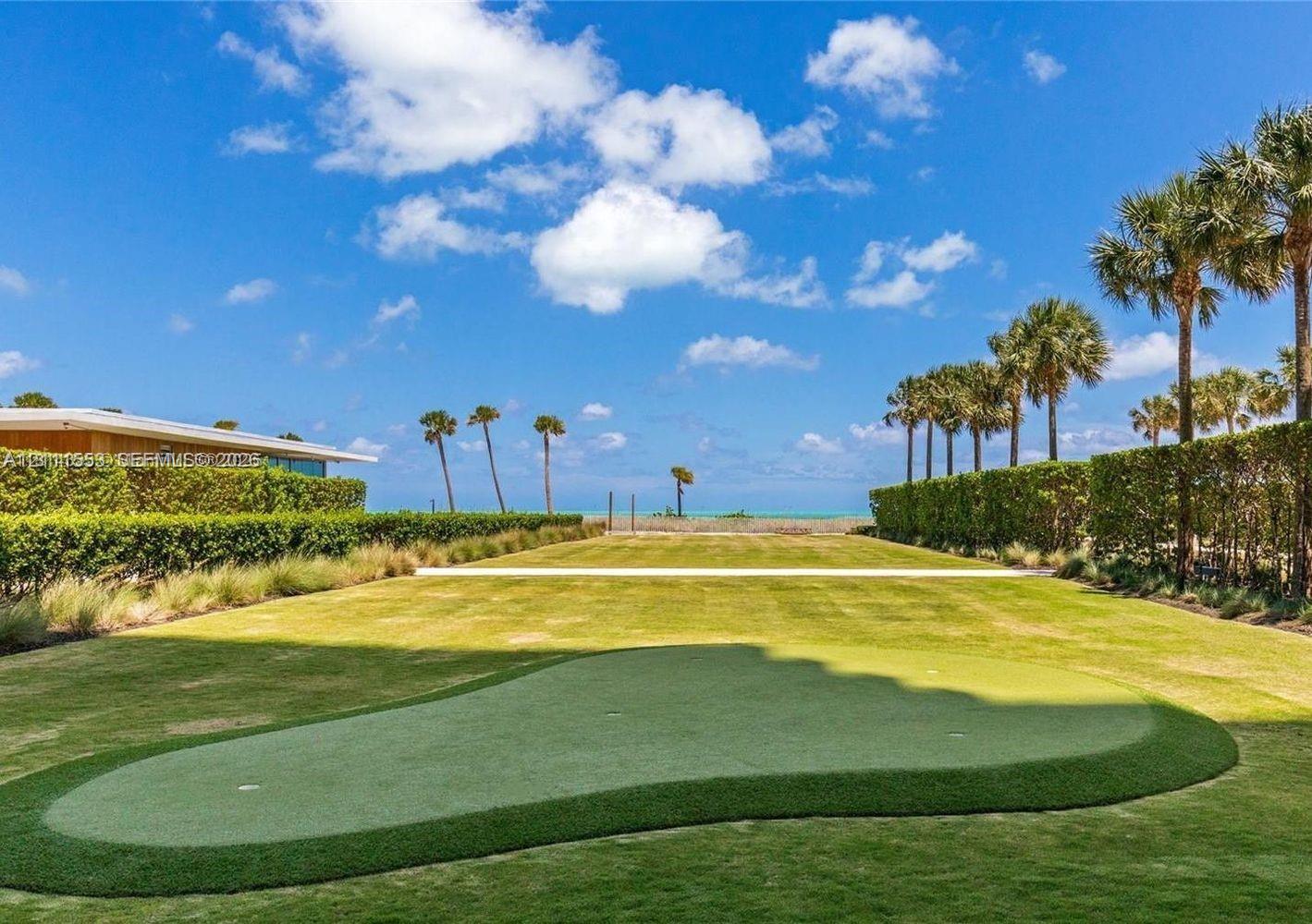 Expansive lawn featuring a built-in putting green, manicured hedge perimeter, and palm trees