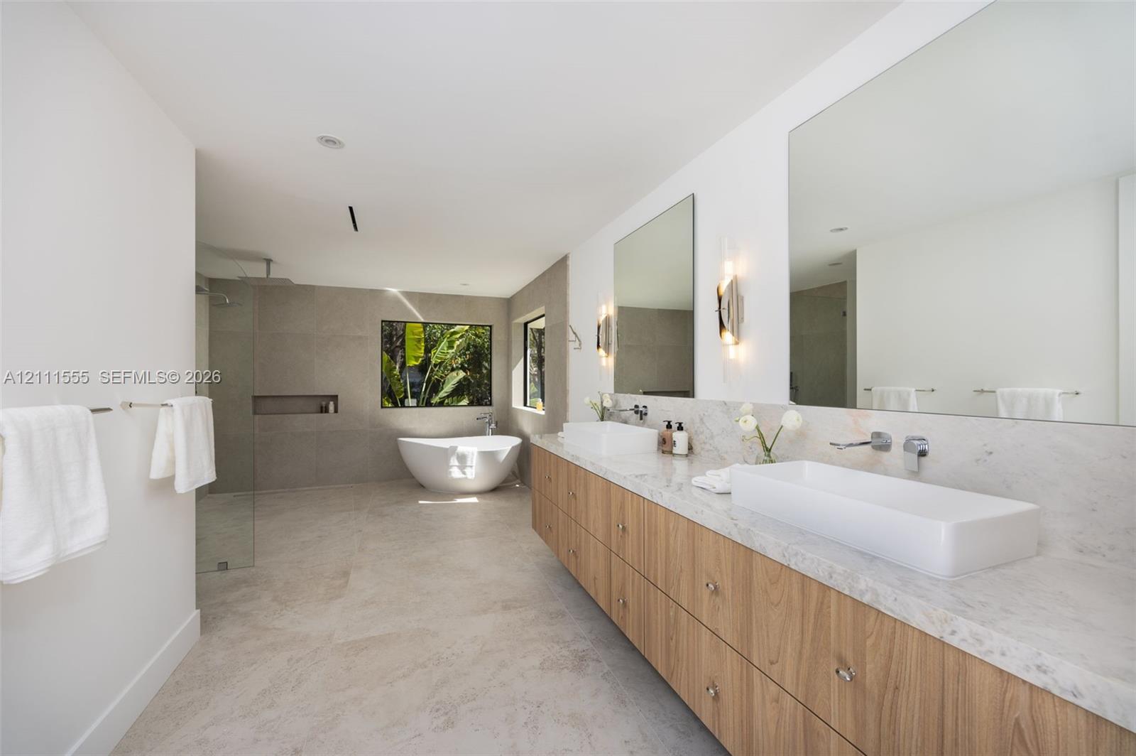 Floating dual vanity with stone-finish countertops, rectangular vessel sinks, wall-mounted faucets, large-format tile flooring, and a freestanding soaking tub