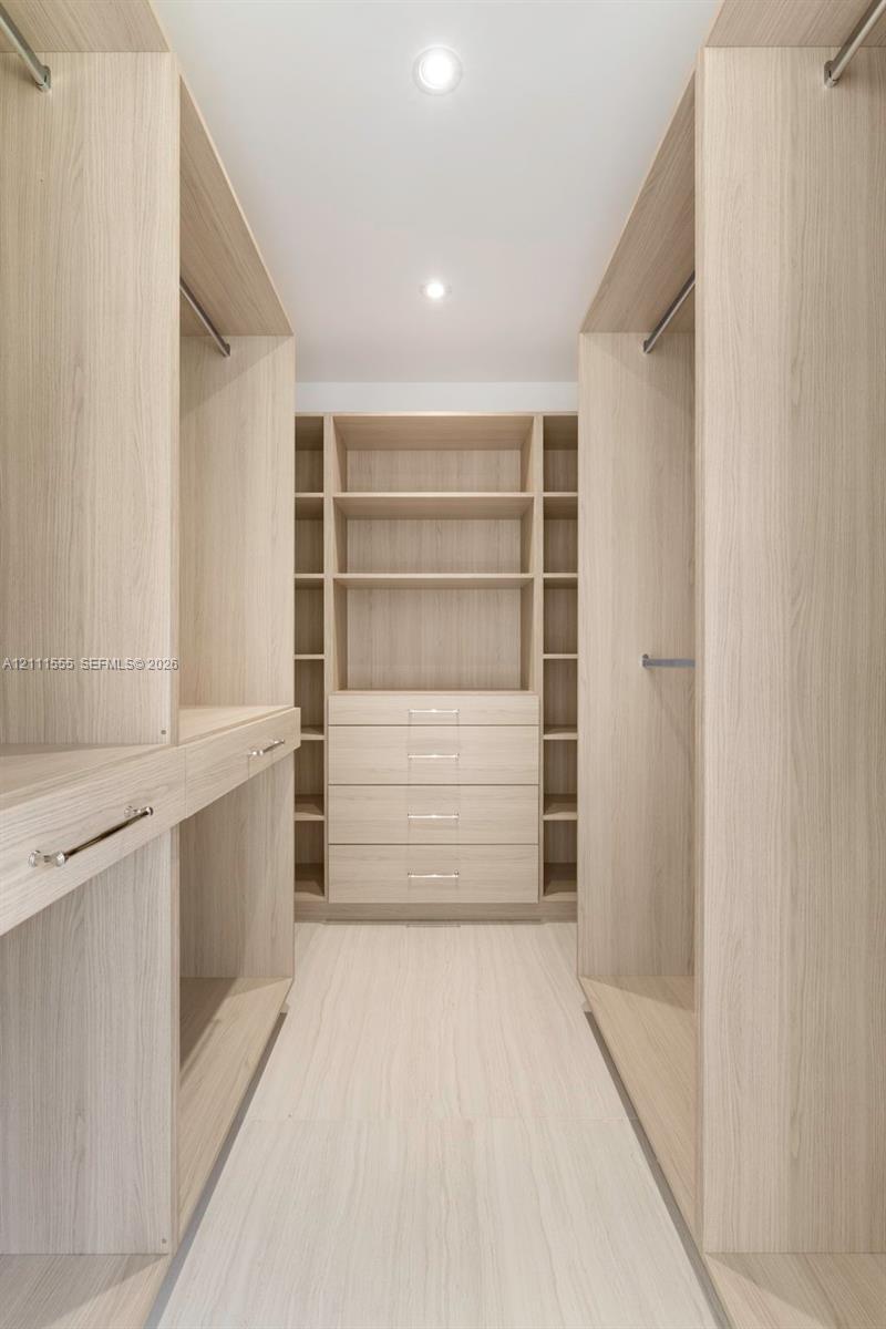 Custom closet organization system featuring light wood-finish cabinetry, built-in shelving, integrated drawers with metallic hardware, and recessed lighting