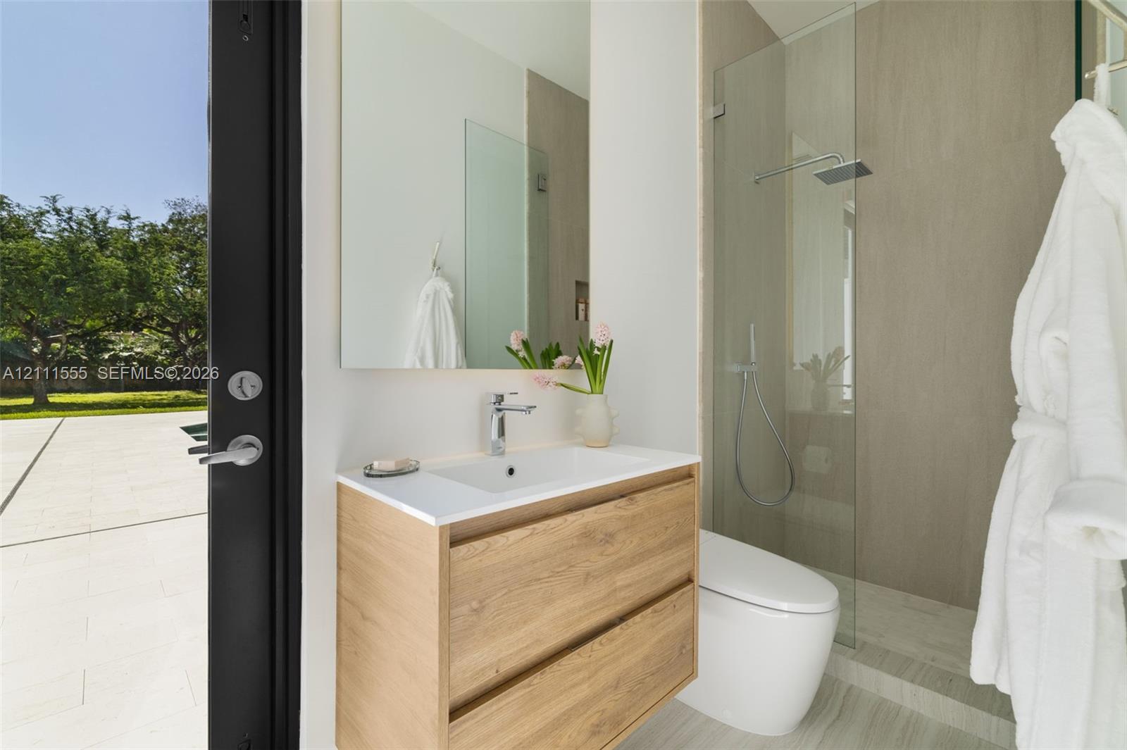 Wall-mounted floating vanity with wood-finish cabinetry, rectangular integrated sink, frameless wall-to-wall mirror, glass-enclosed walk-in shower with rainfall showerhead, and porcelain tile flooring