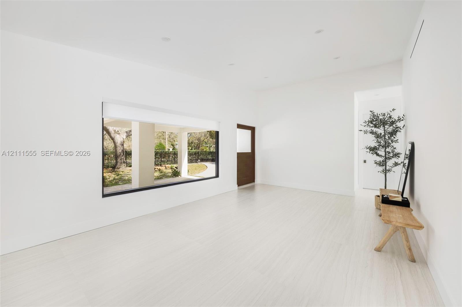 Minimalist interior featuring light-toned flooring, expansive picture window, recessed ceiling lighting, and solid wood door Minimalist interior featuring light-toned flooring, expansive picture window, recessed ceiling lighting, and solid wood door