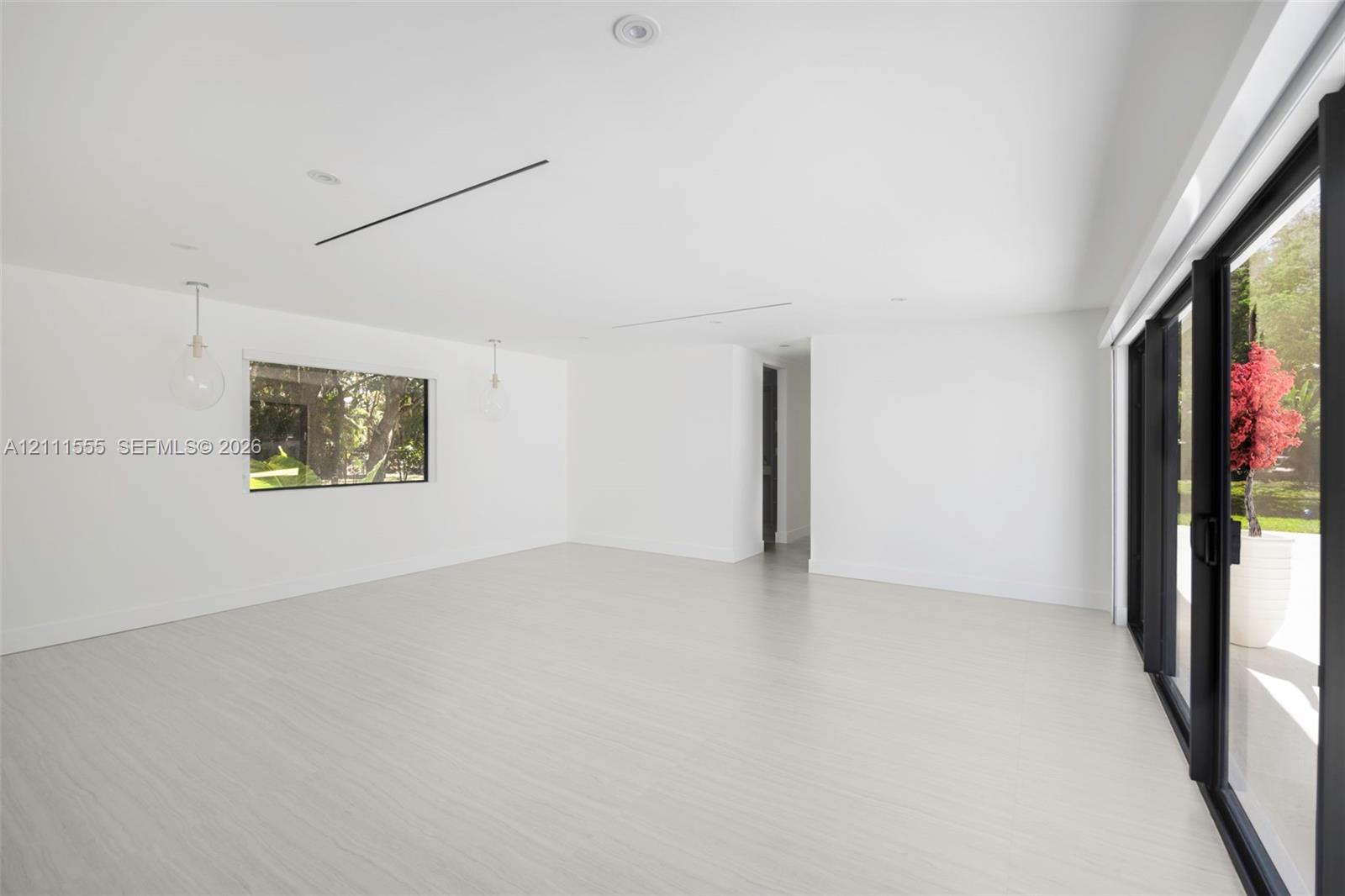 Open-concept interior with light-toned wood-finish flooring, recessed lighting, glass pendant fixtures, and floor-to-ceiling black-framed sliding glass doors