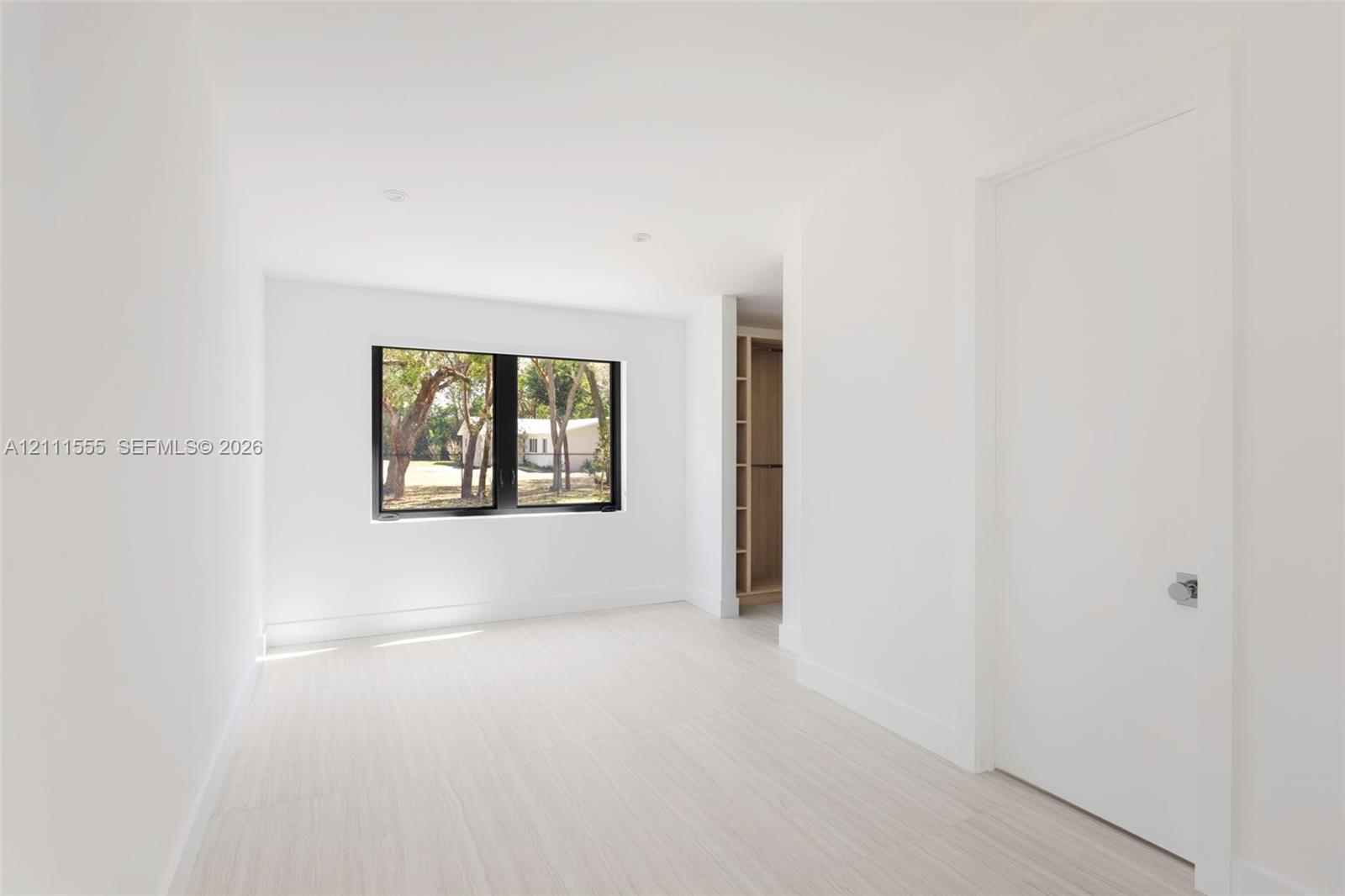 Bright room featuring light wood-finish flooring, a black-framed window, recessed lighting, and built-in closet shelving