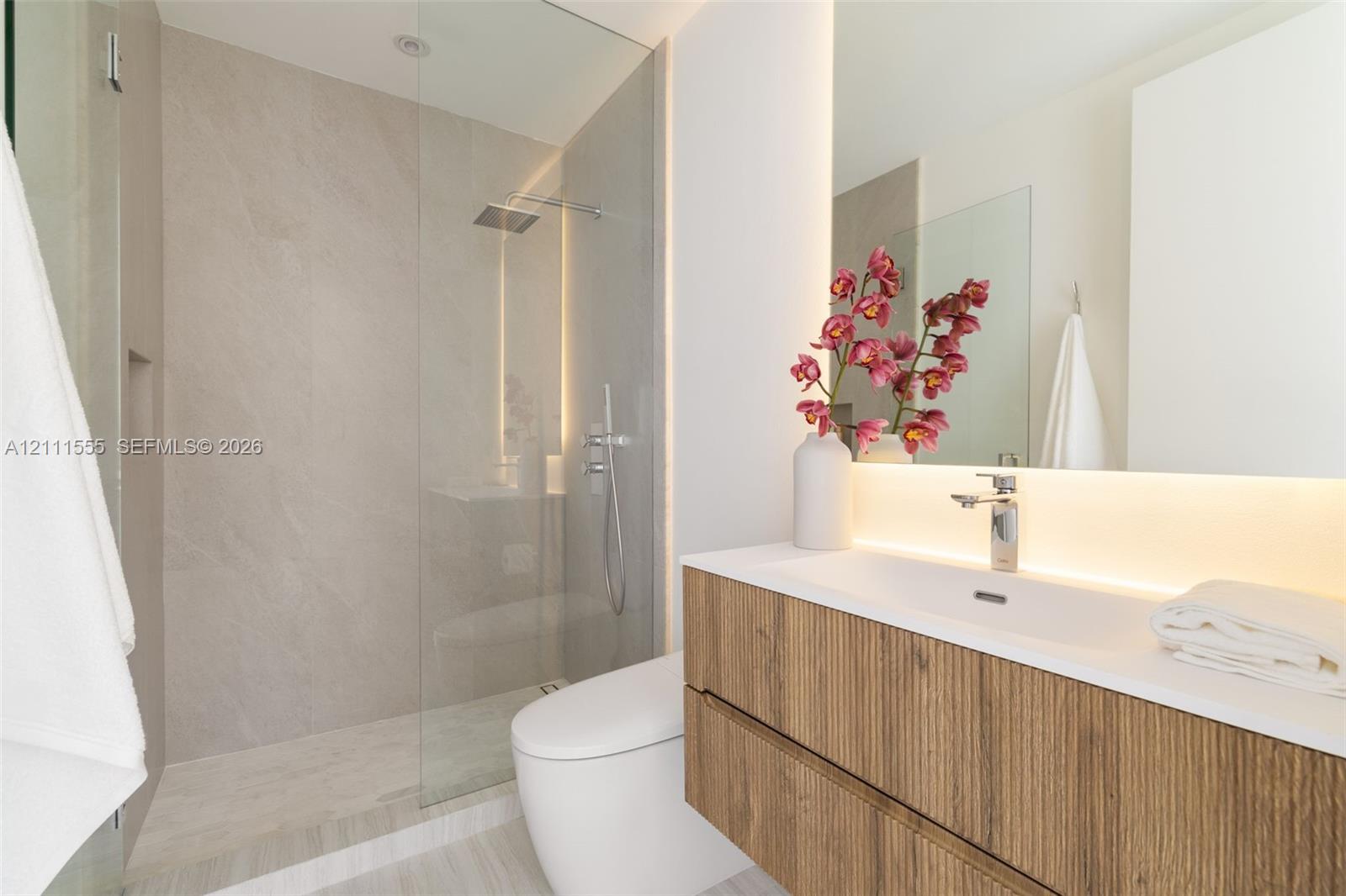 Floating wood-finish vanity with an integrated sink, walk-in glass-enclosed shower featuring large-format tile surround, rain-style showerhead, and integrated backlighting
