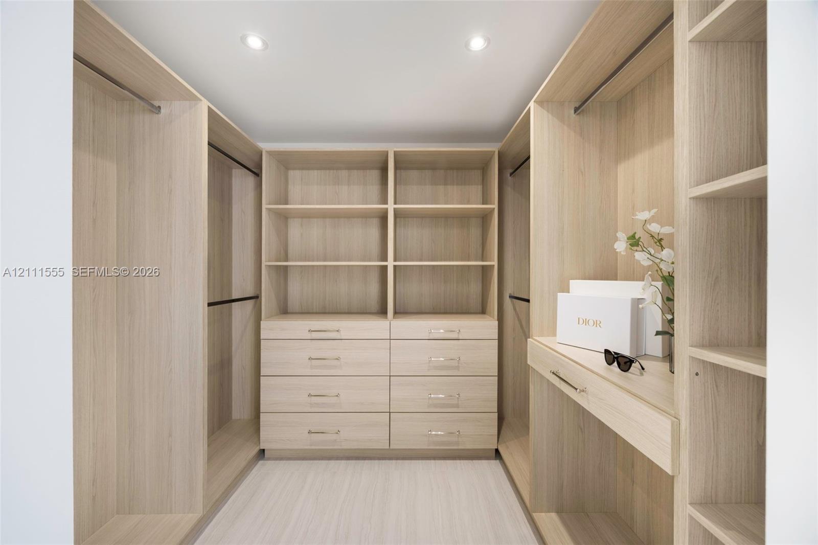 Primary Closet - Hers Custom wood-finish walk-in closet featuring floor-to-ceiling shelving, integrated drawer banks, hanging rods, and recessed lighting