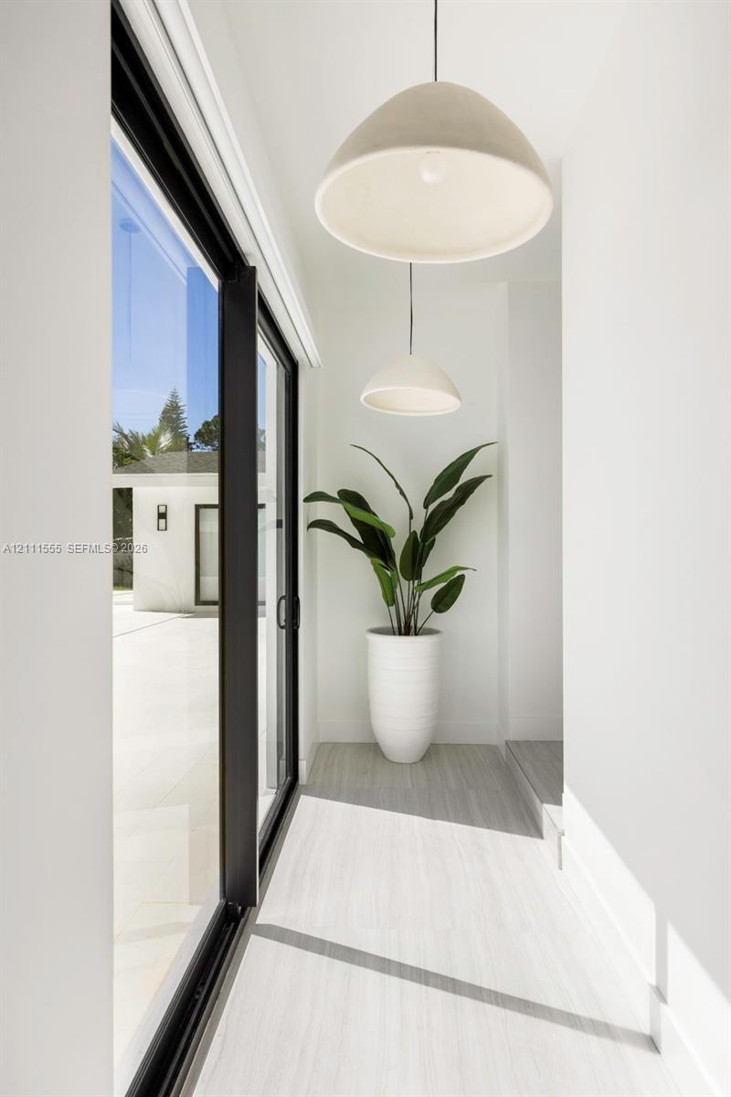 Floor-to-ceiling sliding glass doors with black frames, neutral wood-finish flooring, and dual hemispherical pendant lighting fixtures