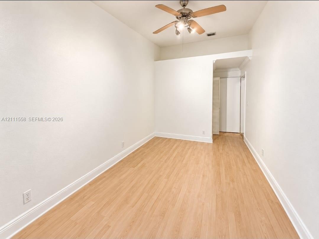 Interior space featuring wood-finish flooring, white walls, and a ceiling fan with integrated lighting
