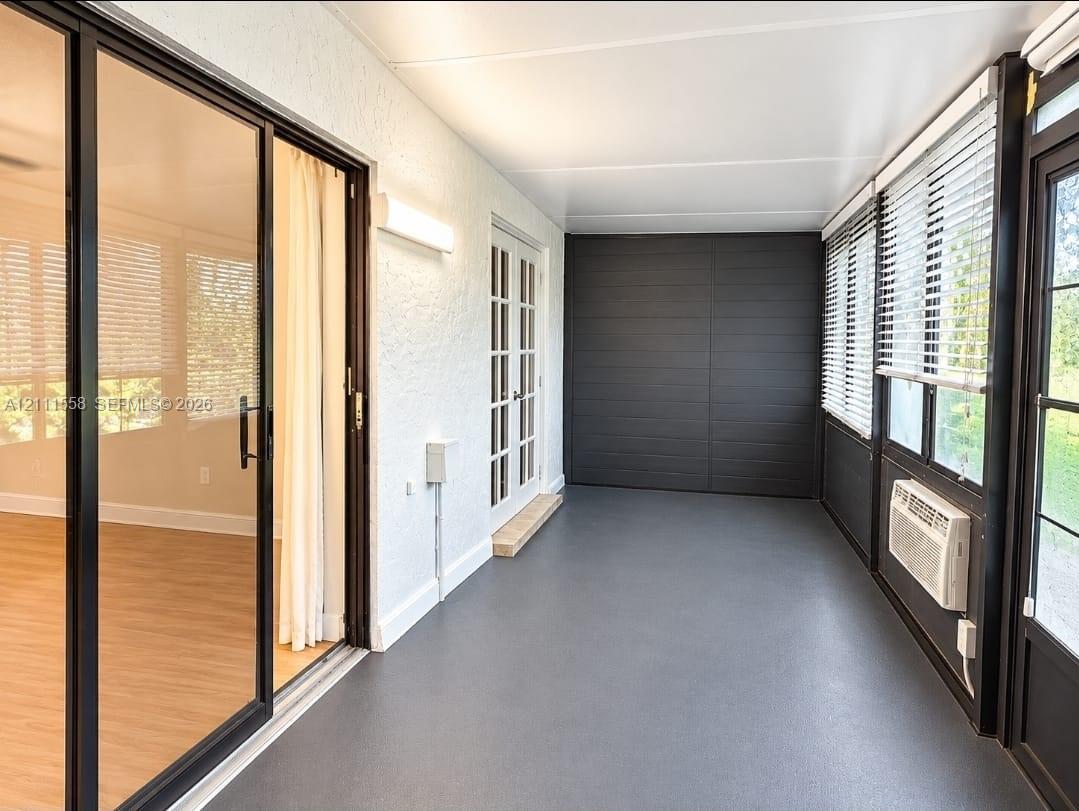Enclosed porch featuring charcoal-toned flooring, expansive glass sliding doors, dual-pane windows with integrated blinds, French entry doors, and a wall-mounted climate control unit