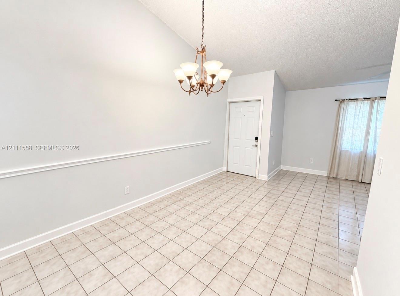 Vaulted ceiling with an overhead chandelier, neutral ceramic tile flooring, and decorative wall molding