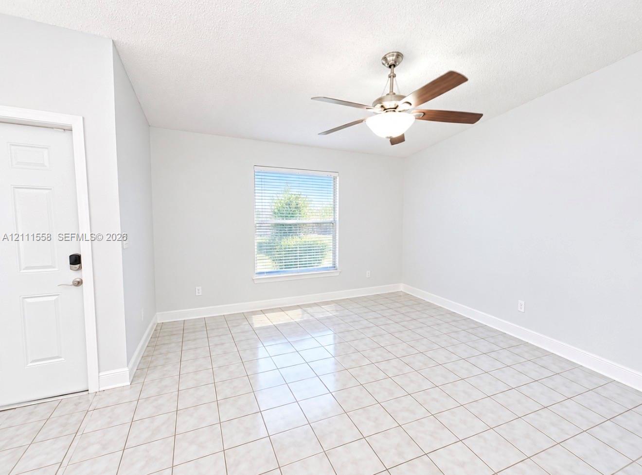 Neutral-toned interior featuring ceramic tile flooring, a brushed nickel ceiling fan with integrated lighting, and a single-panel door with smart-lock hardware