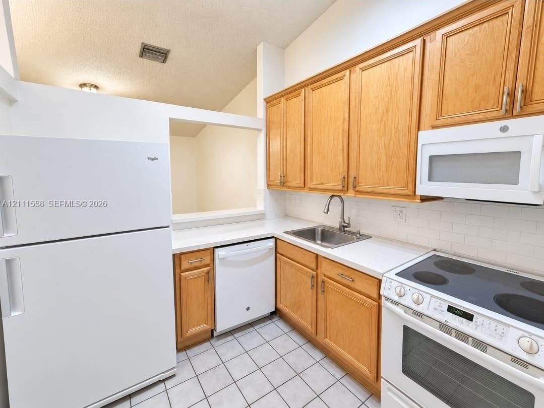 Kitchen featuring natural wood cabinetry, white subway tile backsplash, white solid-surface countertops, ceramic tile flooring, and a stainless steel under-mount sink with a high-arch pull-down faucet