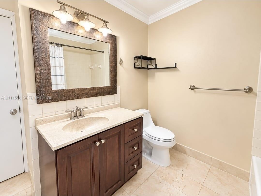 Dark wood-finish vanity with a stone-composite countertop, integrated sink, three-light fixture, framed wall mirror, and neutral tile flooring