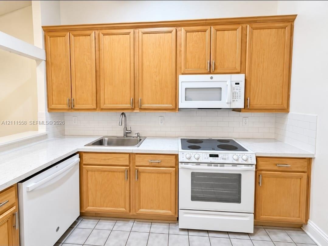 Kitchen featuring light wood-finish cabinetry, white countertops, a white subway tile backsplash, a stainless steel undermount sink, and a white built-in microwave and range