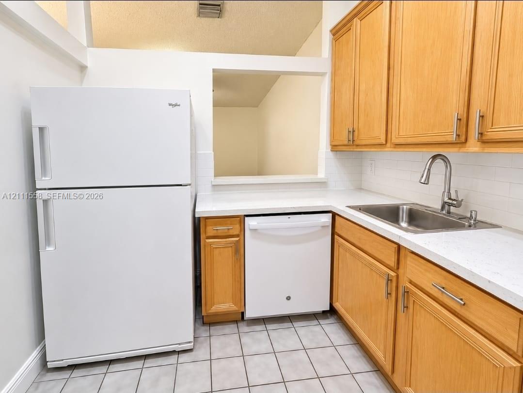 Kitchen featuring wood cabinetry, white countertops, a stainless steel undermount sink with a gooseneck faucet, a white tile backsplash, and ceramic floor tiling