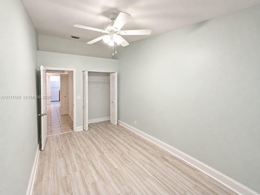 Room featuring wood-finish flooring, a ceiling fan with integrated lighting, and a reach-in closet with double-hinged doors