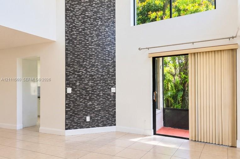 Double-height ceilings, floor-to-ceiling dark stone-tile accent wall, neutral ceramic tile flooring, and sliding glass door with external patio access