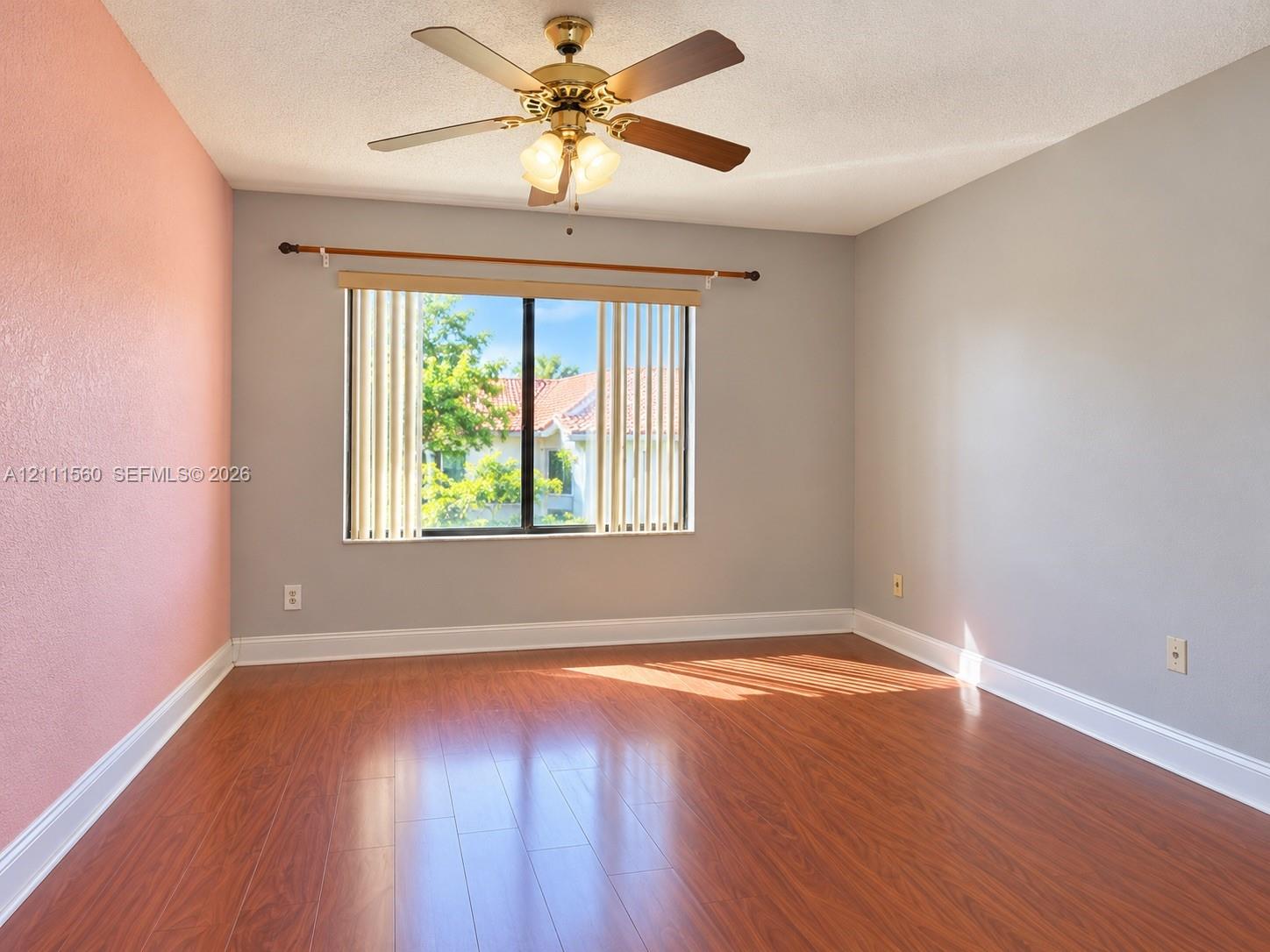 Room featuring wood-finish flooring, a ceiling fan with integrated lighting, and a single window with vertical blinds