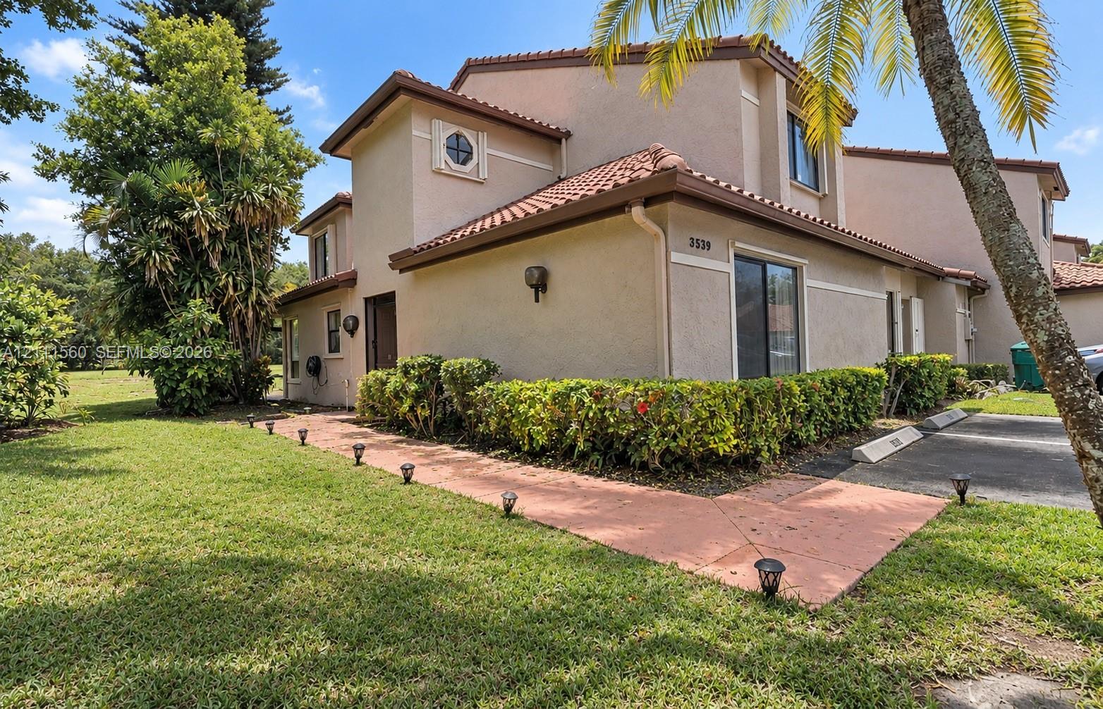 Stucco exterior with a tiled roof, multi-level architectural design, circular accent window, concrete walkway, and landscaped shrubbery Stucco exterior with a tiled roof, multi-level architectural design, circular accent window, concrete walkway, and landscaped shrubbery