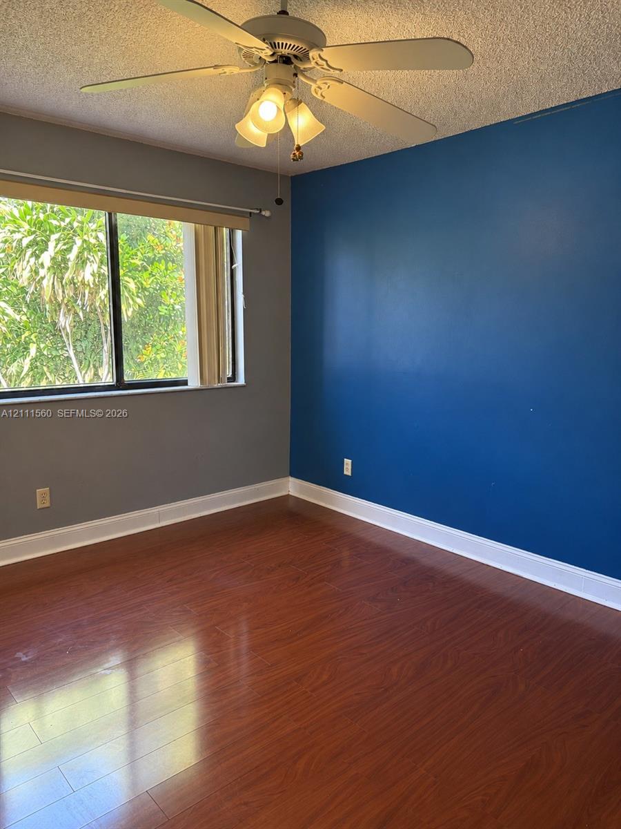 Wood-finish flooring, accent wall, ceiling fan with light fixture, and horizontal window