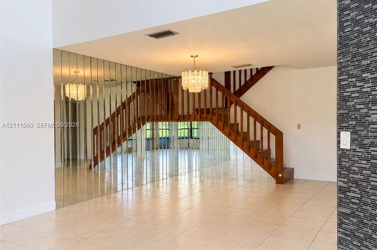 Staircase featuring wood railings and vertical balusters, mirrored accent wall, tiled flooring, tiered glass chandelier, and textured stone-finish wall accent