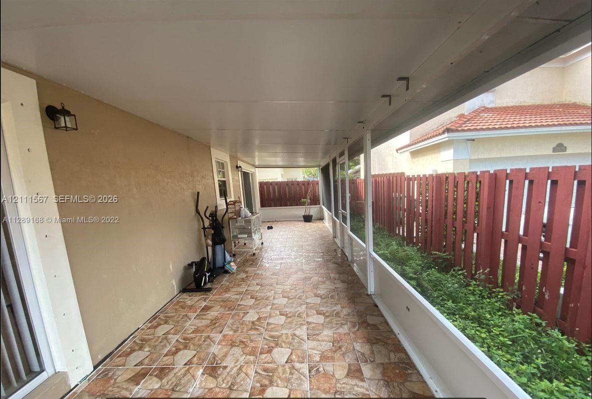 Covered patio featuring stone-patterned tile flooring, a solid ceiling with attached wall-mounted lighting, and screen panel enclosures bordered by a wood-slat fence