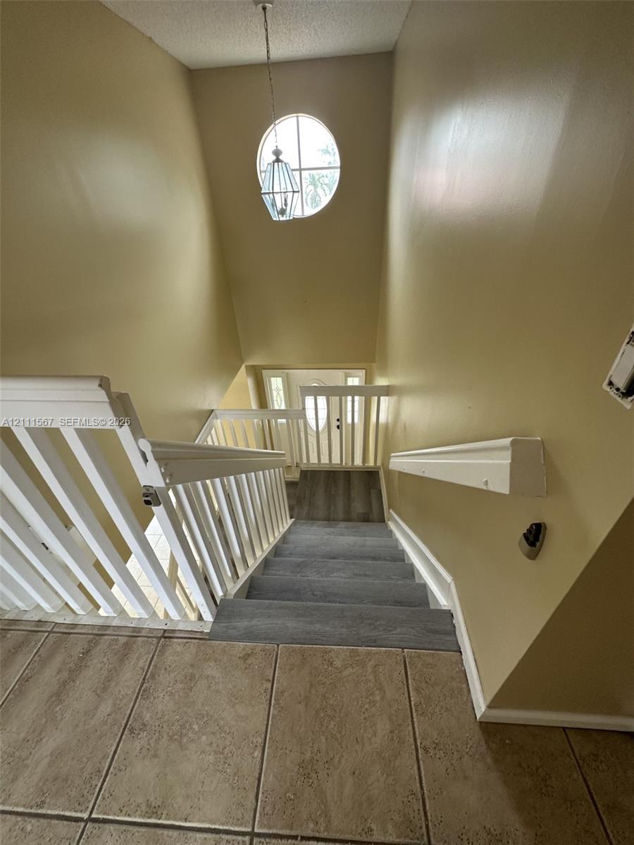 Staircase featuring white balustrades, carpeted treads, a circular accent window, and a hanging pendant light fixture
