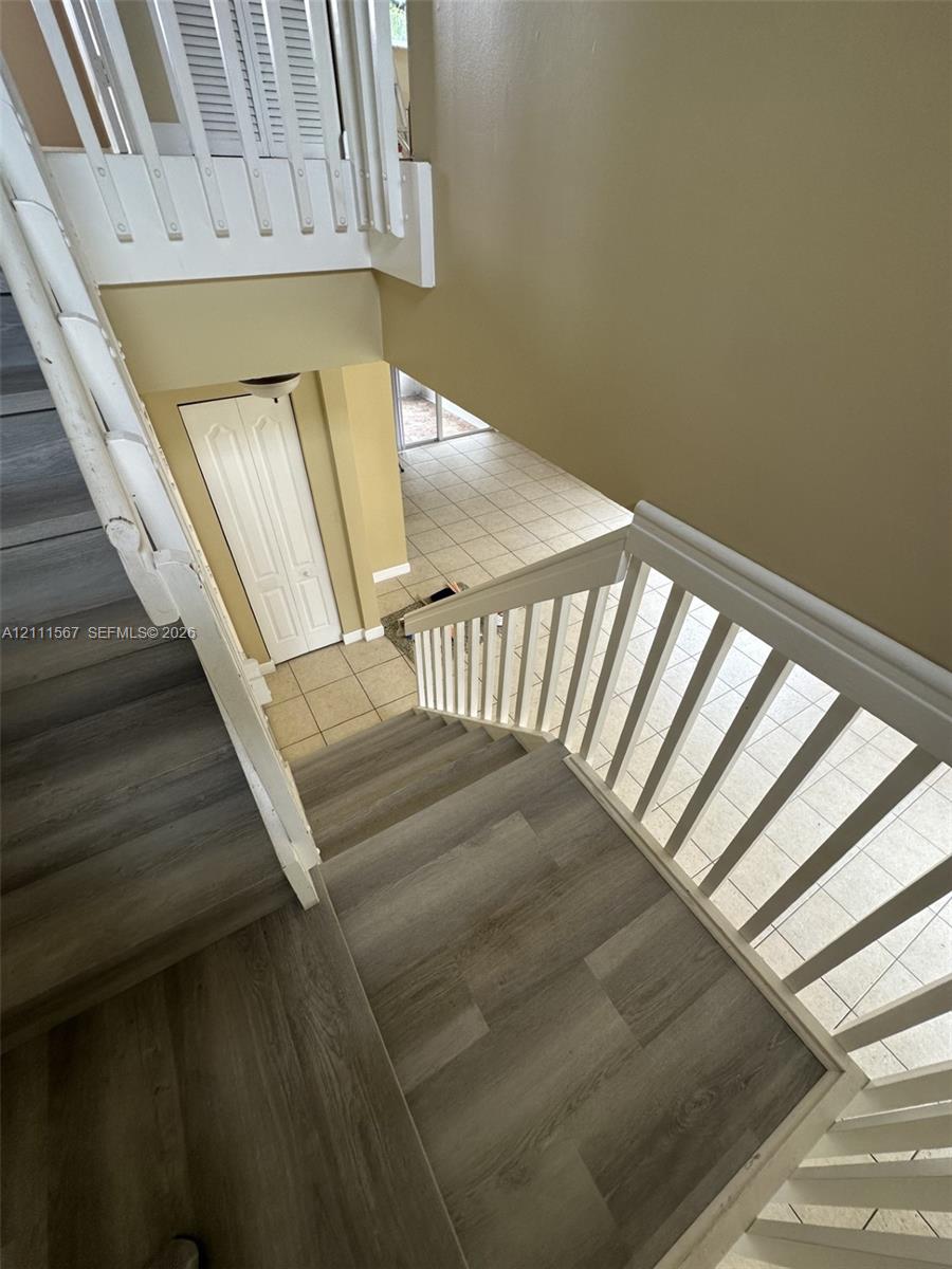 Staircase featuring wood-finish flooring, white wooden balustrades, and ceramic tile flooring on the ground level