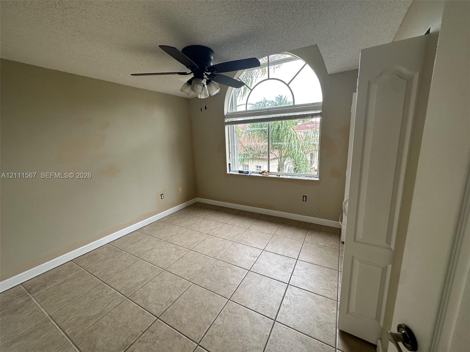 Arched window with decorative muntins, ceramic tile flooring, and integrated ceiling fan with multi-light fixture