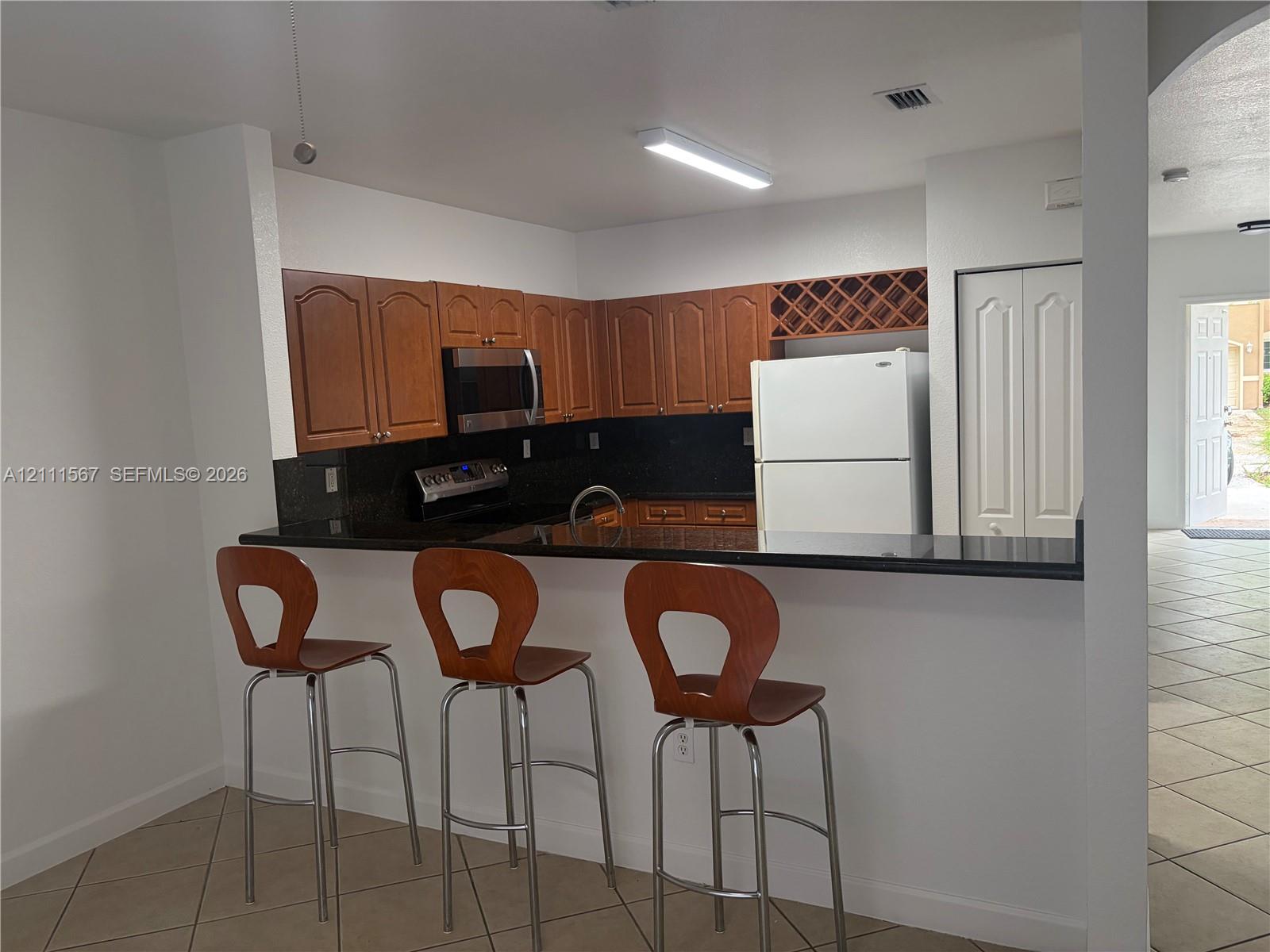 Kitchen featuring dark stone countertops, wood-finish cabinetry, a built-in wine rack, and a breakfast bar