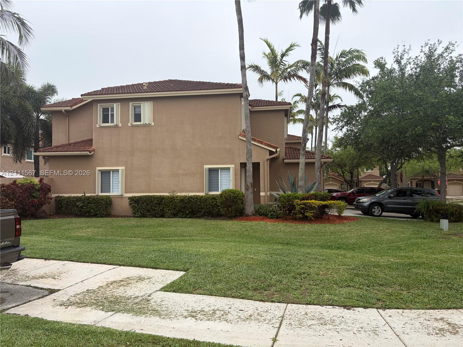 Two-story exterior featuring a stucco facade, clay tile roof, and mature palm trees with manicured landscaping